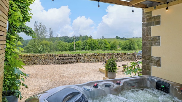A hot tub under a wooden pergola with a stone wall and greenery in the background. - Cherry Tree Cottage (Chesterfield)