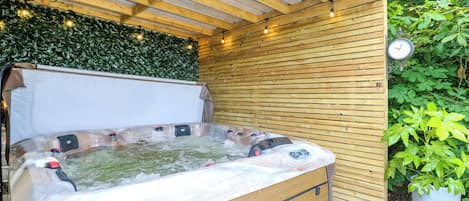 A hot tub with a wooden bench and a wooden roof structure.