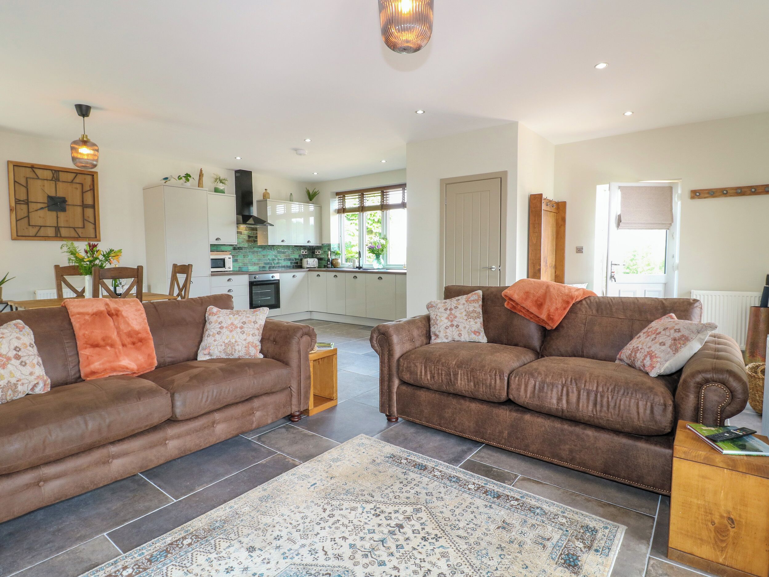 A spacious living room with two brown leather sofas, a patterned rug, and a kitchen in the background.
