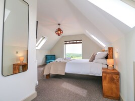 A bedroom with a bed, a chair, a bedside table, a mirror, and a skylight.