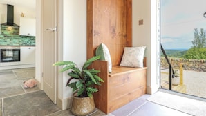 A modern kitchen with a built-in oven, a wooden bench with cushions, and a potted plant. - Cherry Tree Cottage (Chesterfield)