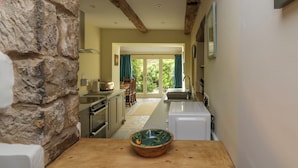 Una cocina estrecha con pared de piedra, vigas de madera y una mesa de madera con un cuenco.