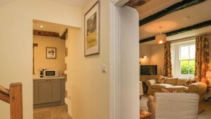 Una sala de estar acogedora con un sofá y un sillón, una zona de cocina con microondas, y un cuadro en la pared.