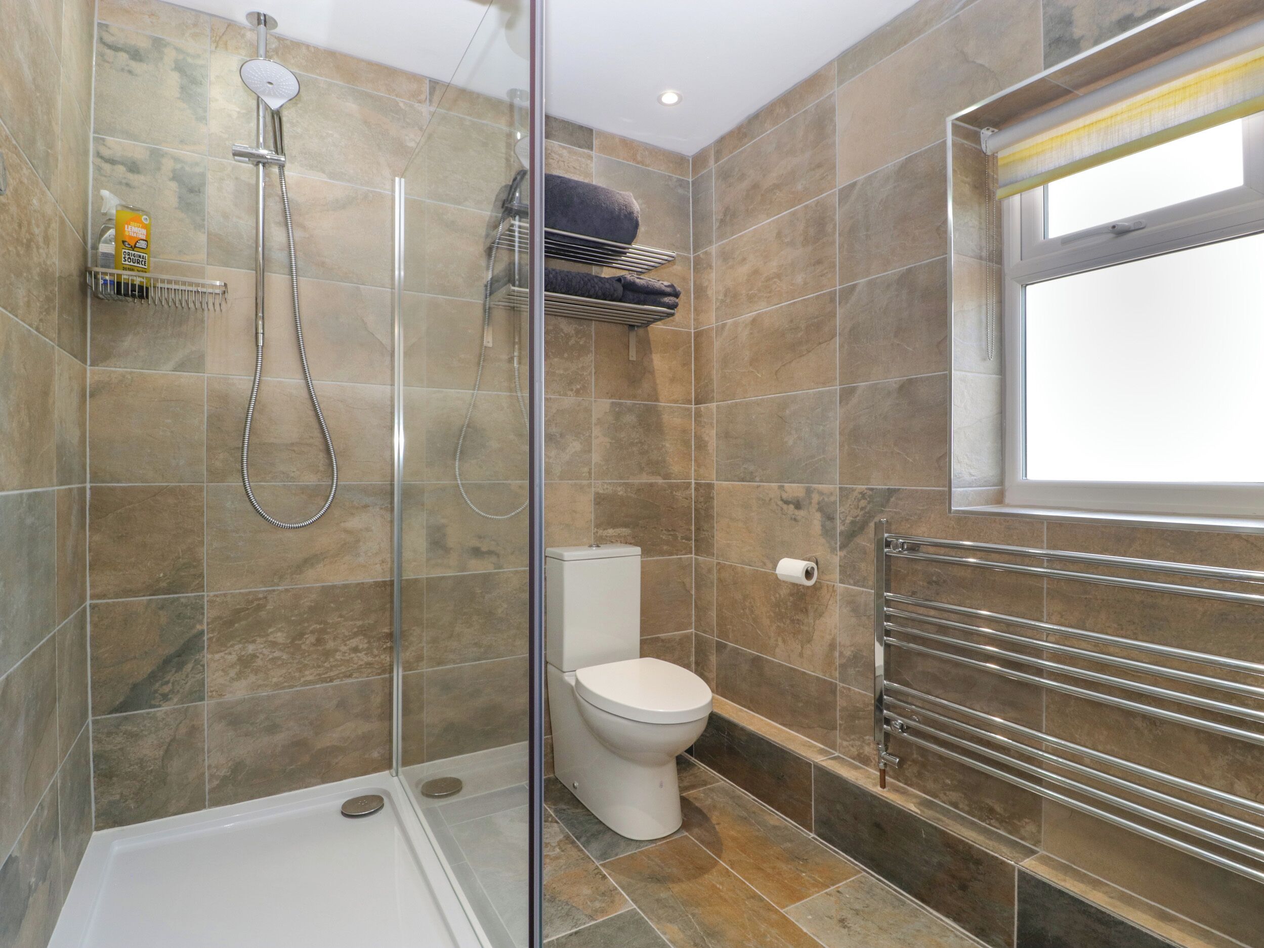 Une salle de bain moderne dotée d’une douche à parois de verre, de toilettes et d’un porte-serviettes.