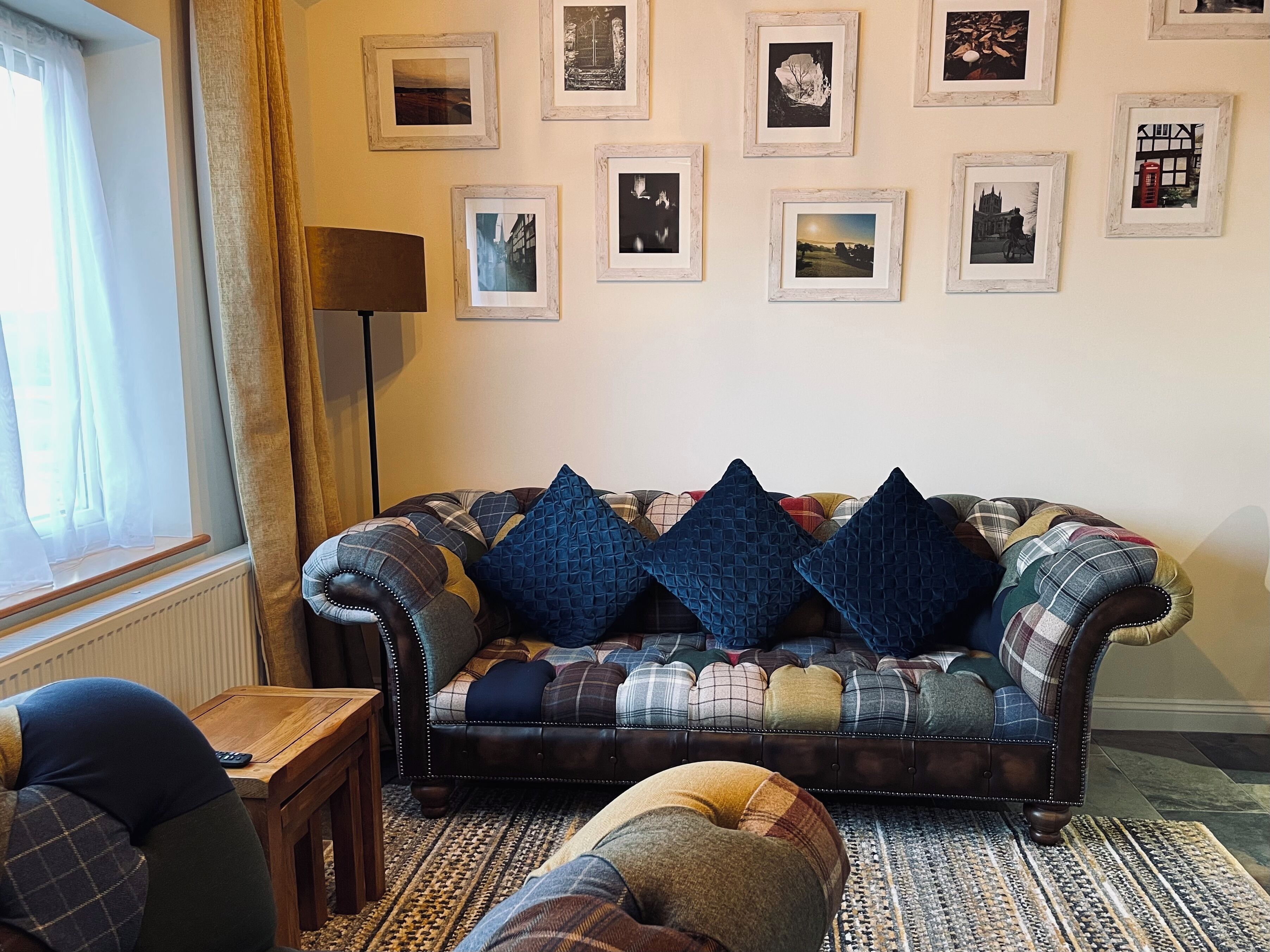 Een woonkamer met een bank, een bijzettafeltje en een vloerlamp. Er hangen ingelijste foto’s aan de muur.