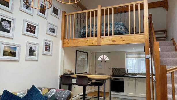 Ein Loft-Wohnbereich mit einer Holztreppe, einem Esstisch mit Stühlen und einer Küche darunter.