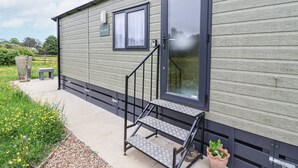 A modern mobile home with a grey exterior, a large sliding glass door, a small window, and a concrete porch with steps. - The Hoot (Stowmarket)