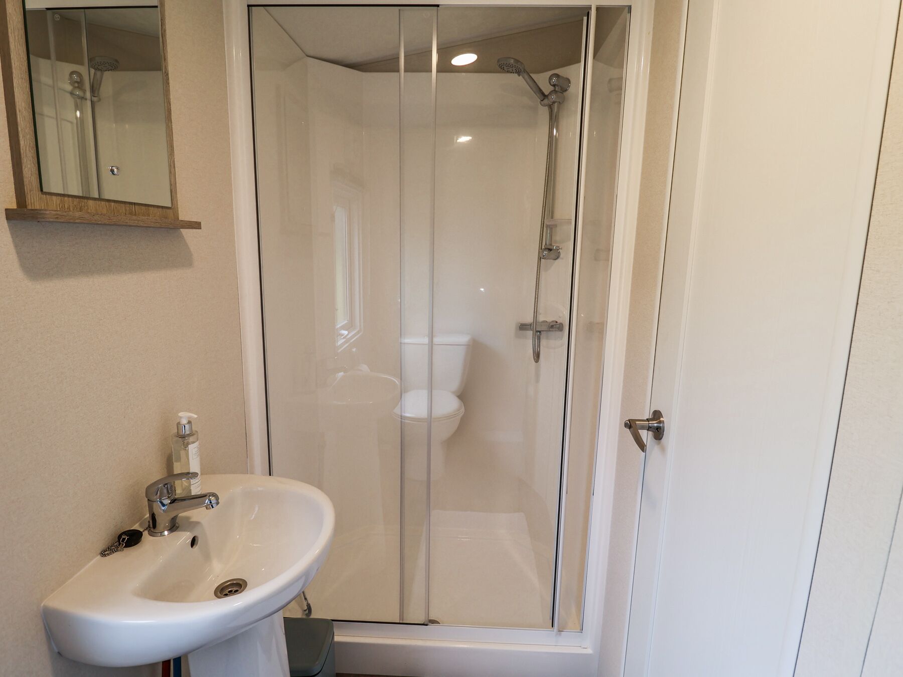 A bathroom with a glass-enclosed shower, a white sink, and a mirror above the sink.
