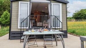 A modern, two-story house with a glass door and windows, a patio with a table and chairs, and a garden view. - The Hoot (Stowmarket)