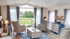 A spacious living area with wicker furniture, a blue patterned rug, and a view of a green garden through large windows. - The Hoot (Stowmarket)