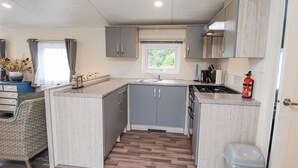 A compact kitchen with grey cabinets, a window, a sink, and a stove. - The Hoot (Stowmarket)