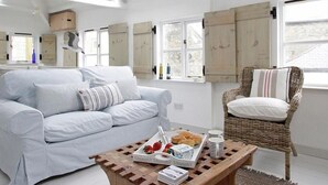 Un salon lumineux avec un canapé bleu clair, un fauteuil en osier et une table basse en bois sur laquelle sont disposés des éléments pour le petit-déjeuner.