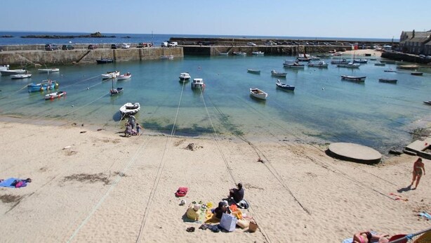 Une plage avec des bateaux ancrés dans l’eau, une rive sablonneuse et une jetée en arrière-plan.