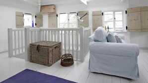 Une pièce lumineuse et blanche, avec un plafond haut et des fenêtres de toit, un berceau blanc, un canapé bleu clair, des paniers en osier et des meubles en bois.