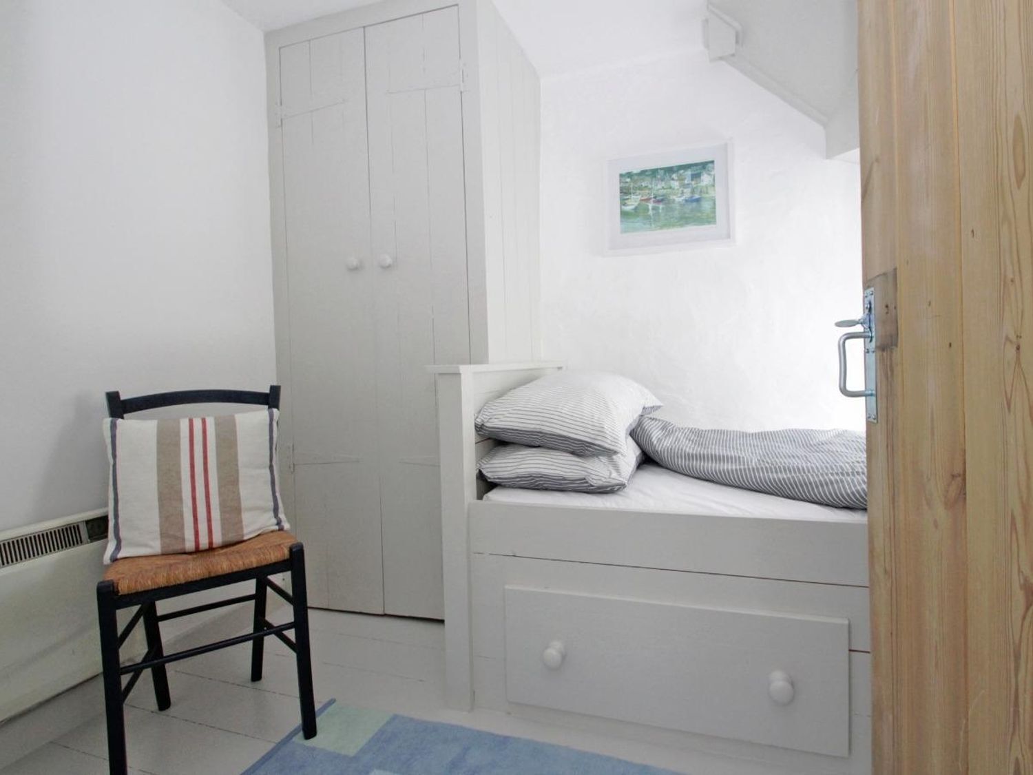 Une petite chambre blanche, avec un lit simple, une chaise et une armoire.