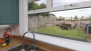 A kitchen with a large window, a sink, and a view of a backyard with a wooden fence and a barbecue area.