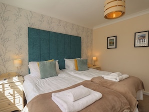 A hotel room with a large bed, two bedside tables, a headboard, and two framed pictures on the wall.