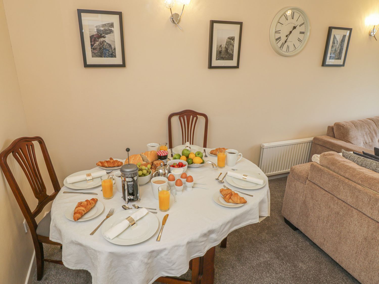 A dining area with a table set for breakfast, including croissants, fruits, and beverages.