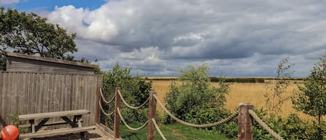 A wooden structure with a picnic table and rope barrier, overlooking a field.
