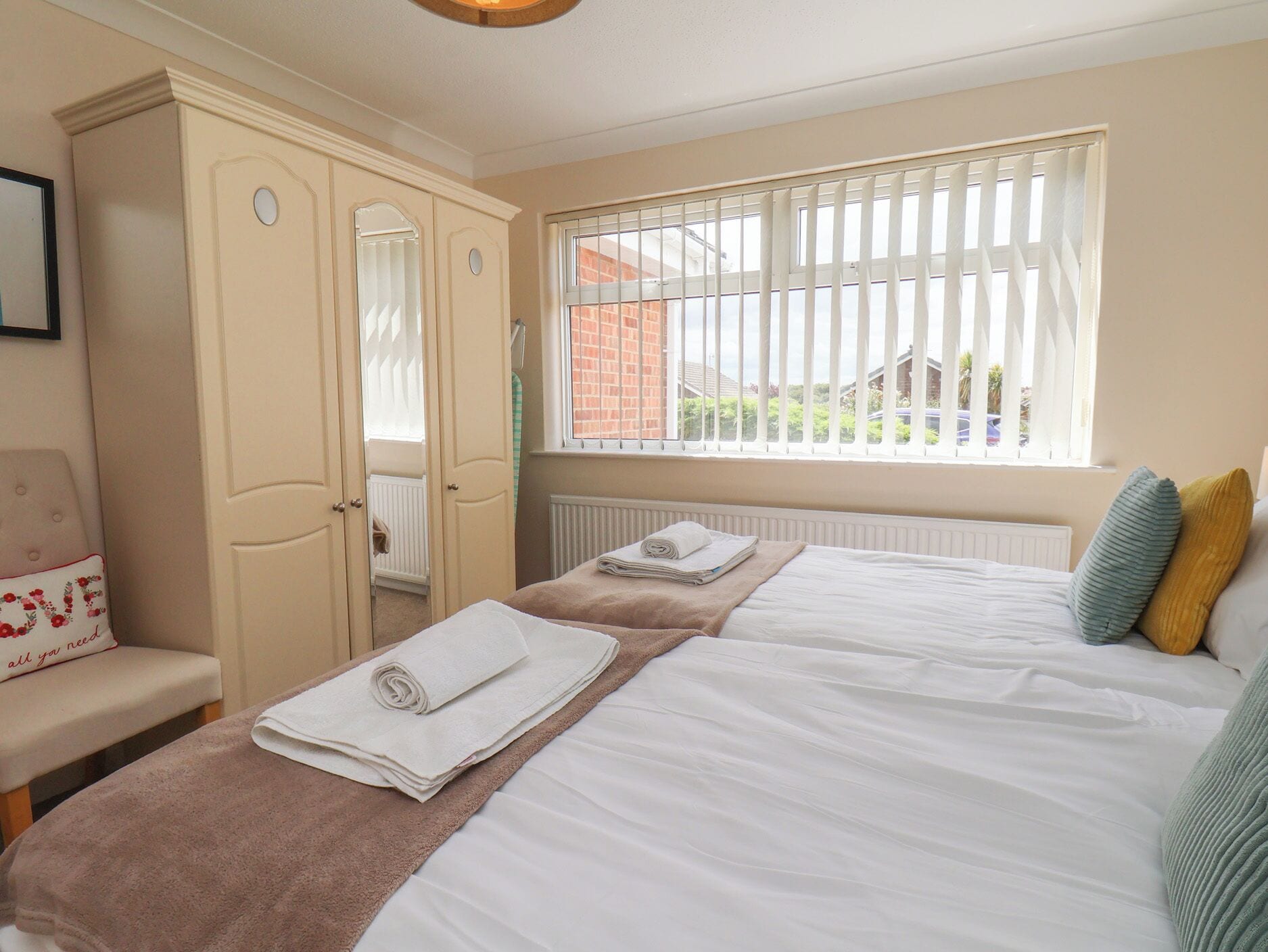 A bedroom with two beds, a window with blinds, a radiator, and a wardrobe.
