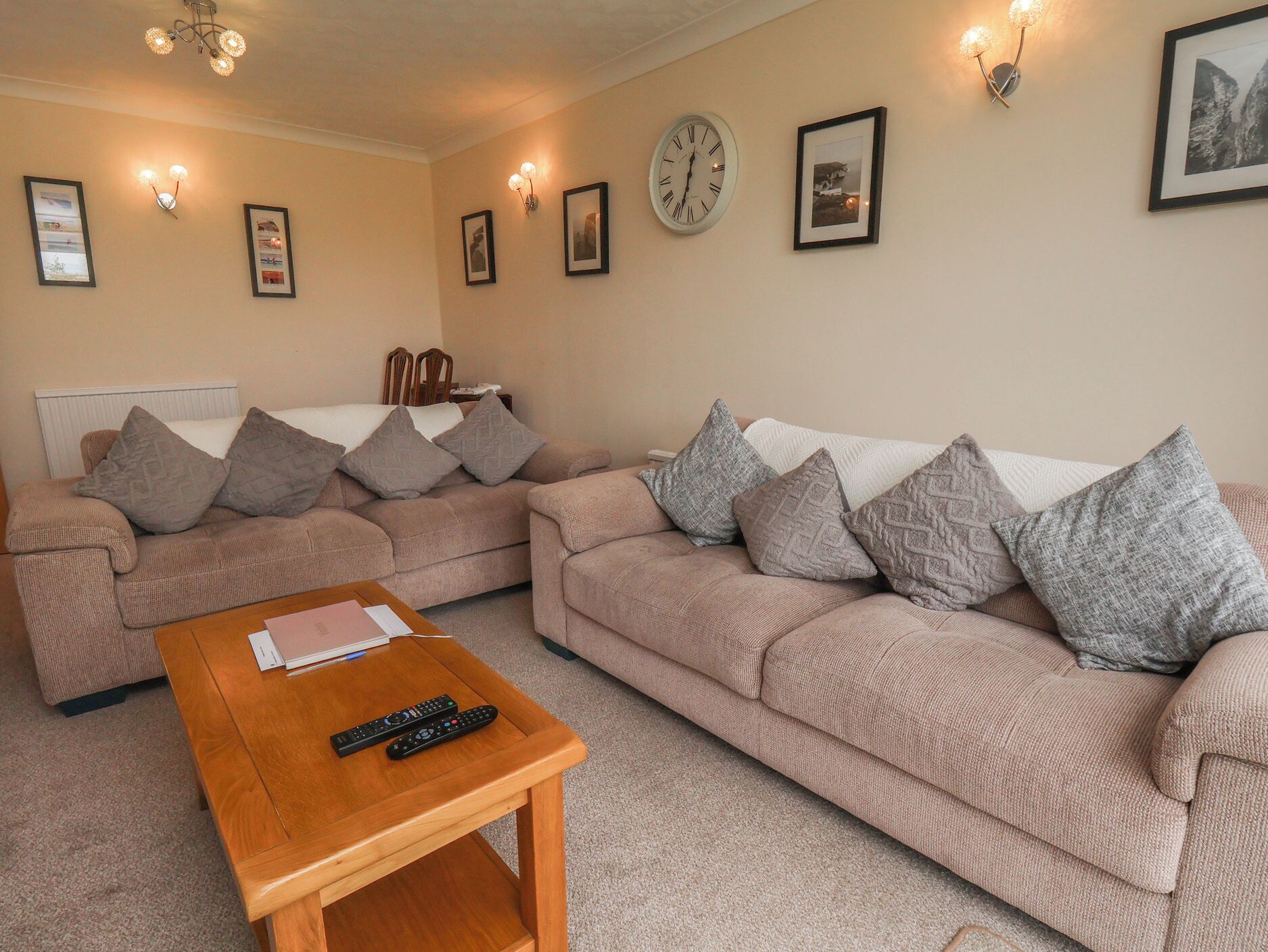 A living room with two sofas, a coffee table, a clock, and wall-mounted lights.