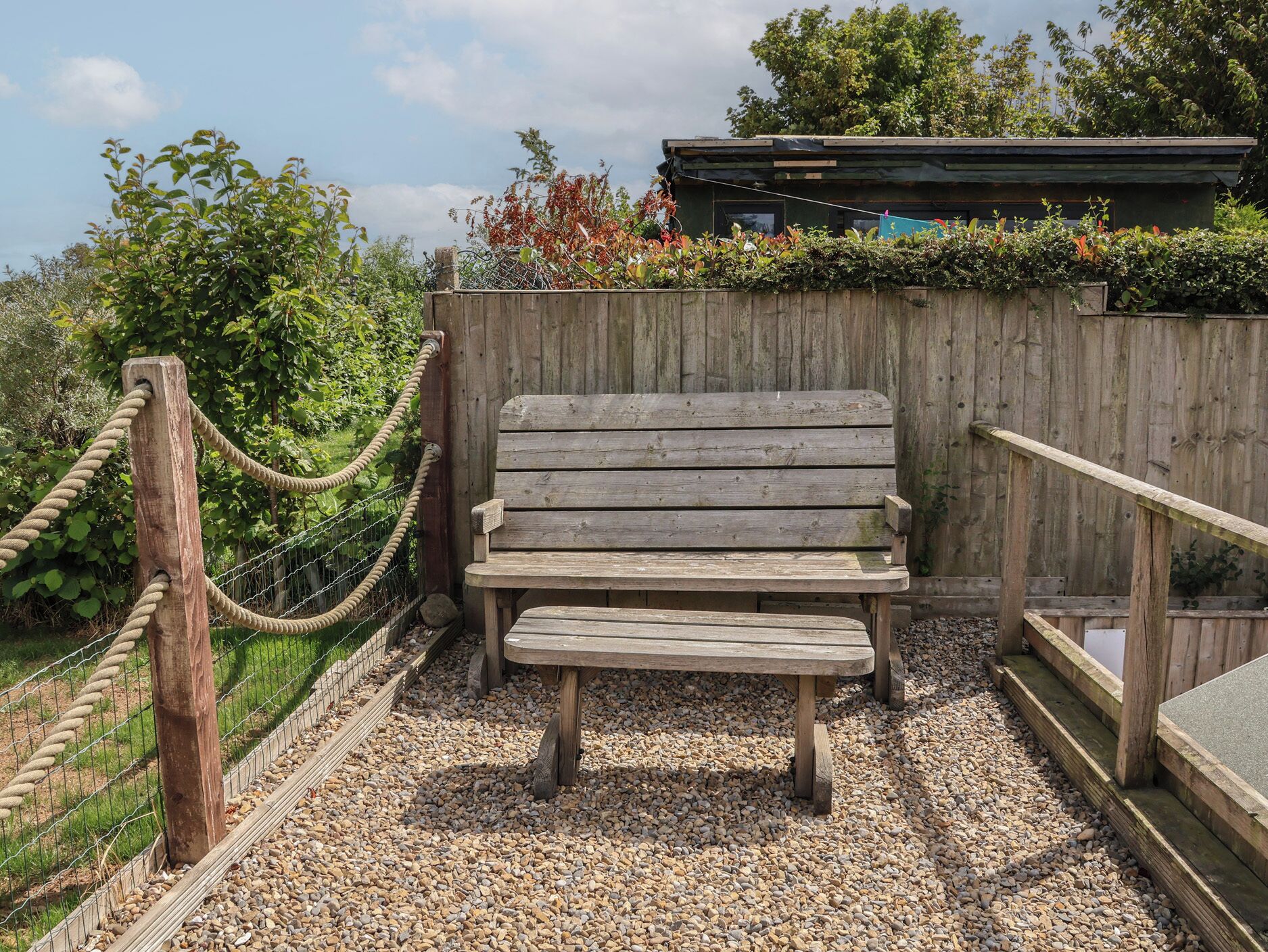 A wooden bench in a garden area with a wooden fence and a rope barrier.