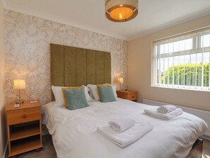 A hotel room with a large bed, two bedside tables, a window with a view, and a ceiling light fixture. - Sea Roke (Filey)