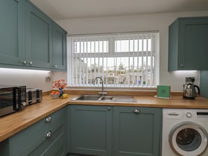 A compact kitchen with a washing machine, a toaster, and a window with blinds.