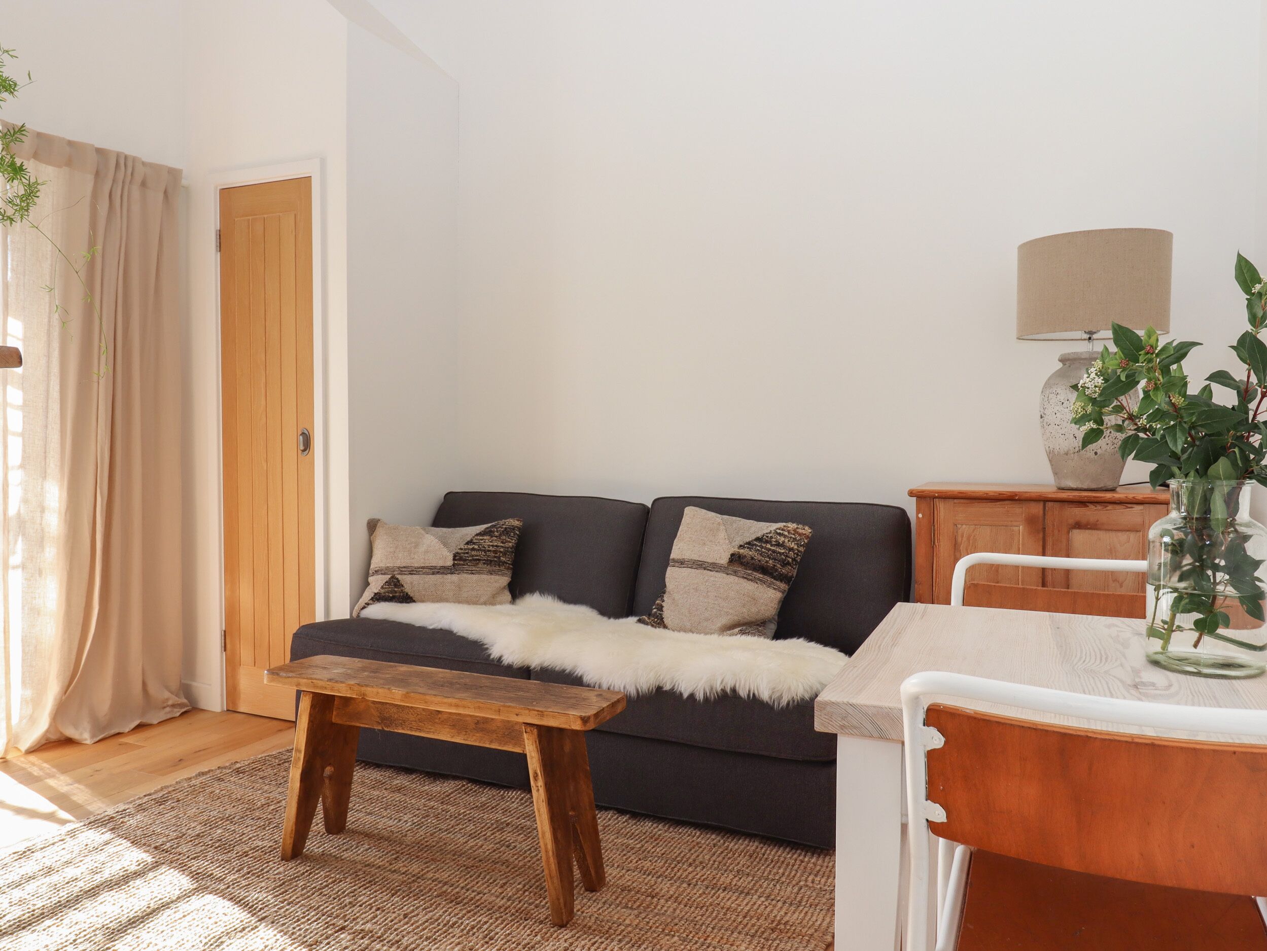 Una sala de estar acogedora con un sofá oscuro, un banco de madera, una mesita y una lámpara sobre un mueble.
