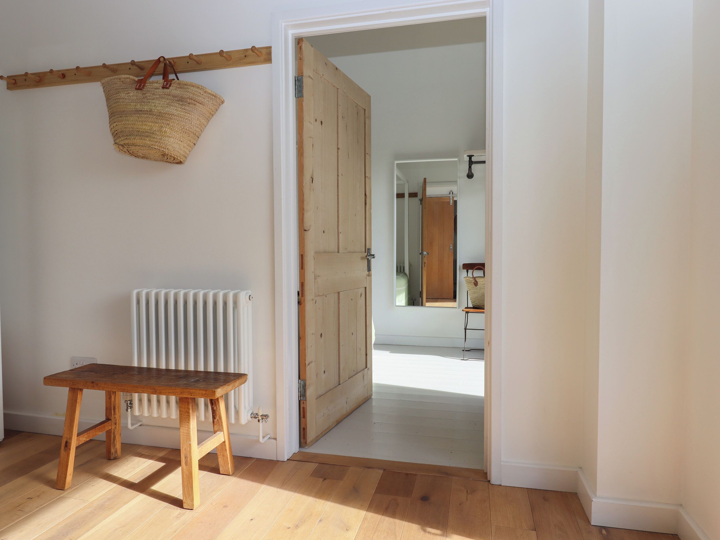 A room with a wooden bench, a radiator, a wooden door, and a hanging basket.