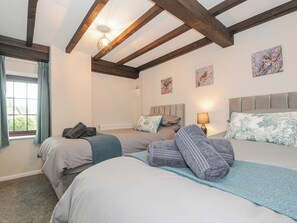 Een slaapkamer met twee bedden, een raam met gordijnen, houten balken en kunstwerken aan de wanden.