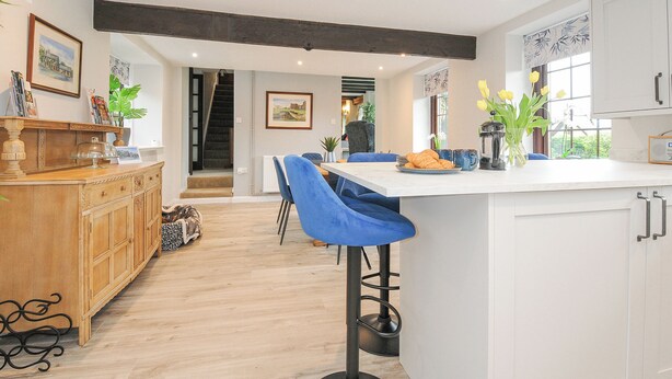 A modern kitchen with a central island, bar stools, and a dining area. - Manor Barn (Saltash)