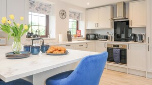 A modern kitchen with white cabinets, a marble countertop, and a blue chair. There is a vase with yellow flowers on the counter. - Manor Barn (Saltash)