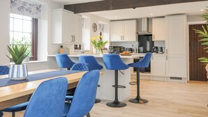 A modern kitchen with white cabinets, a central island, and blue bar stools. - Manor Barn (Saltash)
