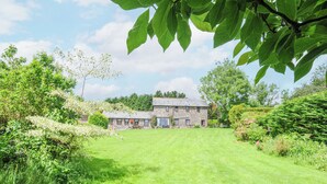 A stone building with a grassy lawn in front, surrounded by trees and shrubs. - Manor Barn (Saltash)