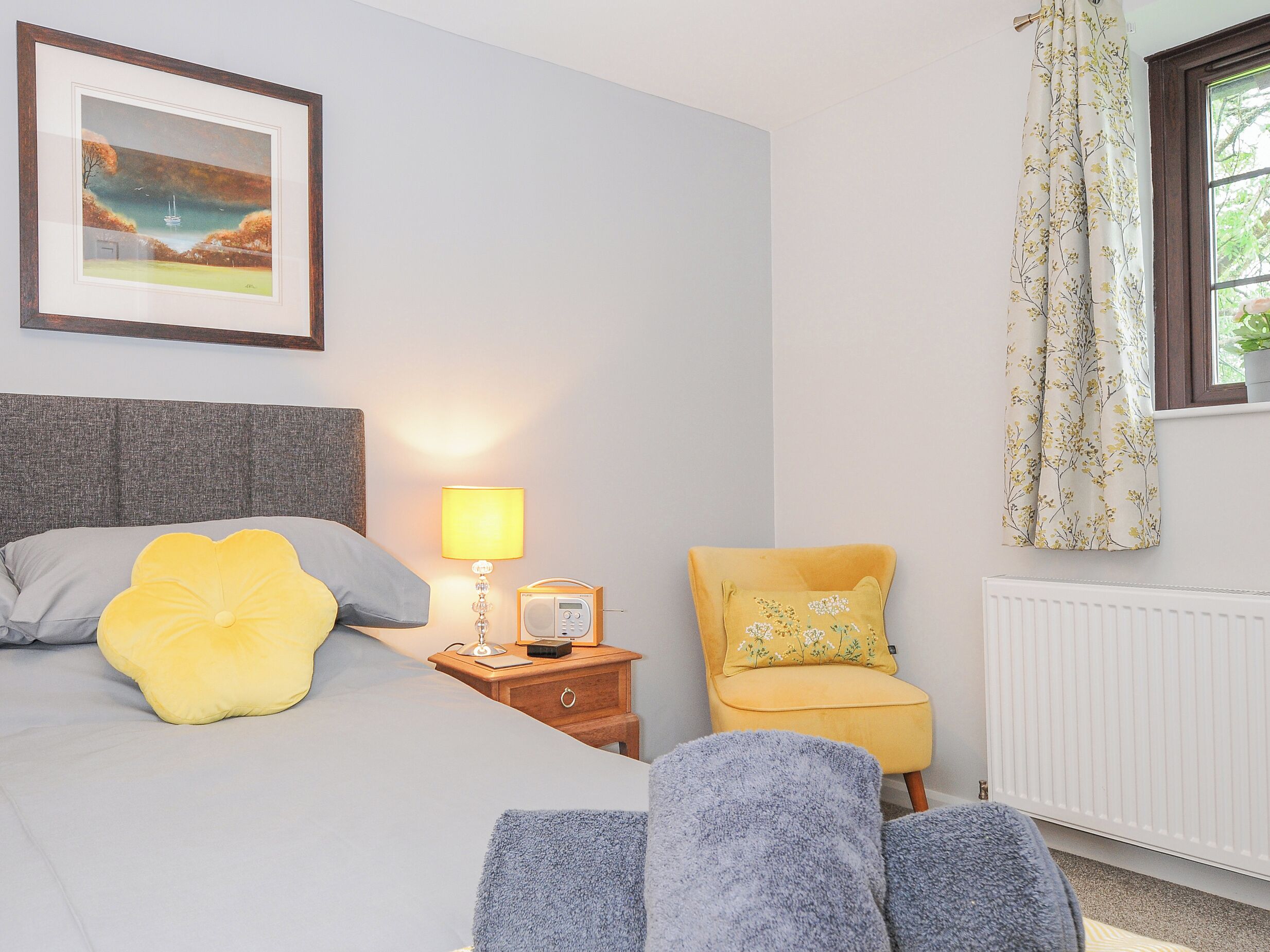 A bedroom with a bed, bedside lamp, radio, chair, and a window with curtains.