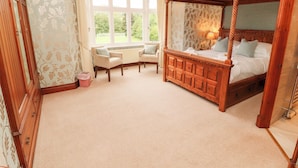 A bedroom with a four-poster bed, two armchairs, a window with a view of greenery, and a chandelier. - Bracken Howe (Ambleside)