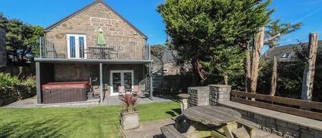 A stone house with a balcony, a hot tub, and a wooden deck with benches.