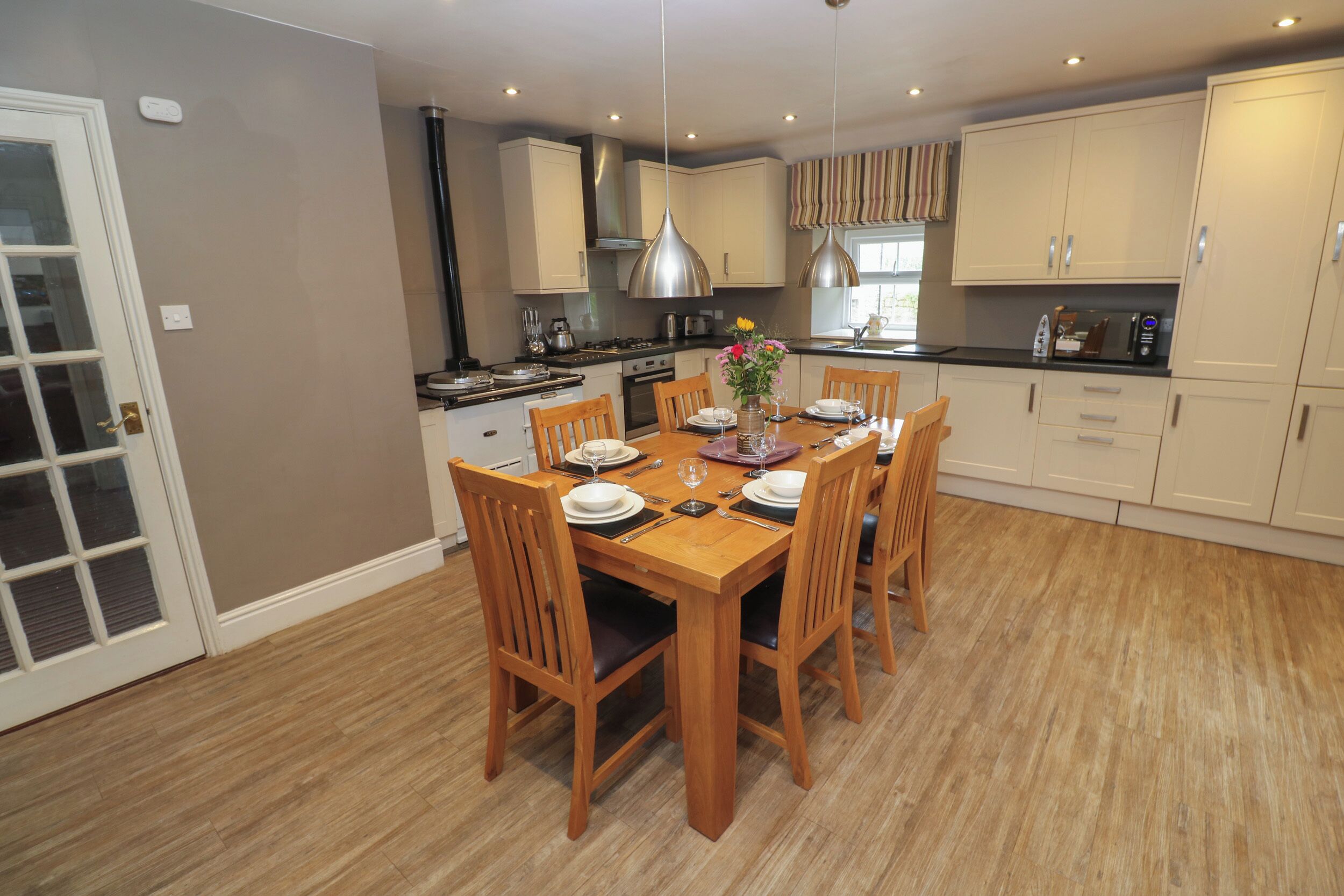 A dining area with a wooden table set for four, surrounded by wooden chairs.