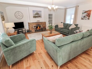 A living room with green sofas, a fireplace, a clock, and artwork on the walls. - Tremornah (Penzance)