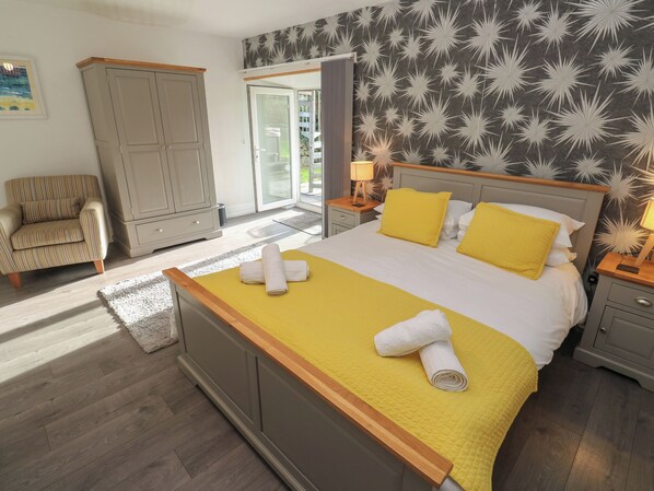 A bedroom with a bed, a chair, a wardrobe, and a view of the outdoors. - Tremornah (Penzance)