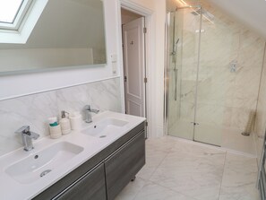 Un baño con dos lavamanos, un espejo grande y una ducha con cerramiento de vidrio.