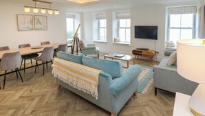 A modern living room with a sofa, a dining table, and a TV. - Amelia's Point (St Ives)