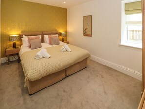 Un dormitorio ordenado con una cama grande, dos mesitas de noche con lámparas, una ventana con vistas y una pared con diseño.