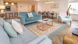 A modern living room with a blue sofa, a coffee table, and a dining area with a table and chairs. - Amelia's Point (St Ives)