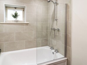 A modern bathroom with a glass-enclosed shower, a white bathtub, and a small window with a plant. - Holborn Cottage, Blencathra Street (Keswick)