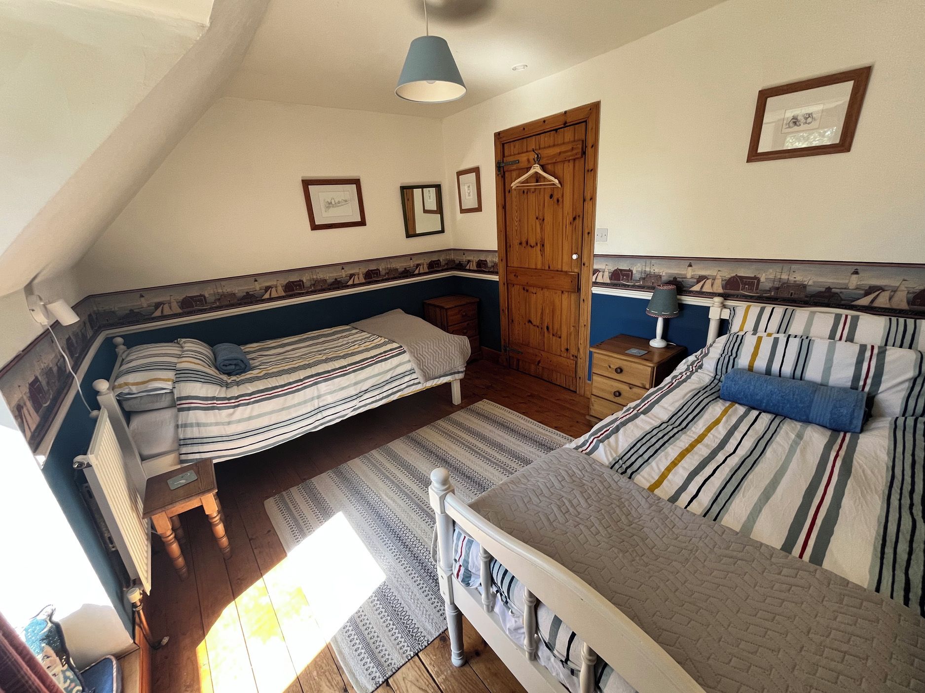 A bedroom with two beds, a wooden door, and a hanging light fixture.
