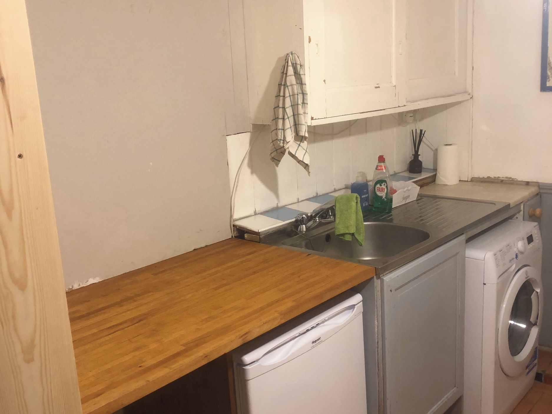 Una cucina compatta con un piano di lavoro in legno, una lavatrice e un lavandino.