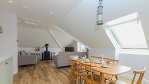 A dining area with a wooden table and chairs, a grey sofa, and a TV in the background. - Daphne (Helston)