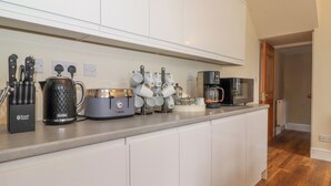 A modern kitchen with white cabinets, a coffee maker, a kettle, and a set of knives. - Melbreak House 2 (Keswick)